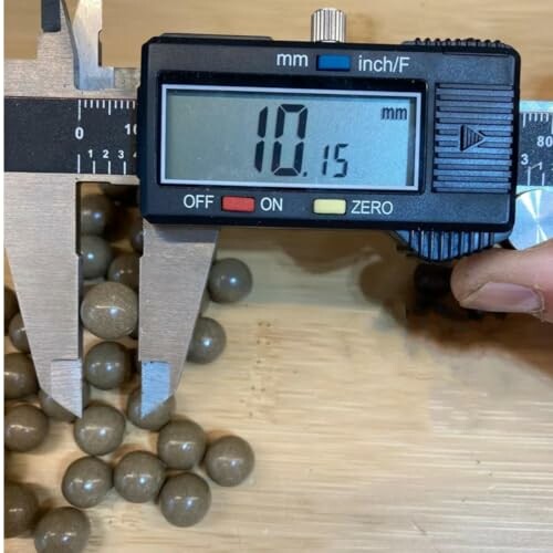 Digital caliper measuring small round balls on a wooden surface.