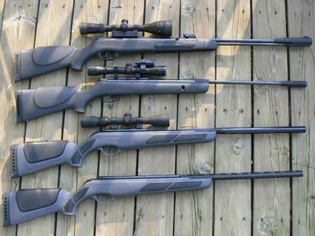 Four rifles with scopes lying on a wooden deck.