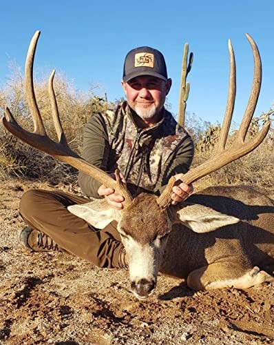 Man holding deer antlers in a desert landscape.